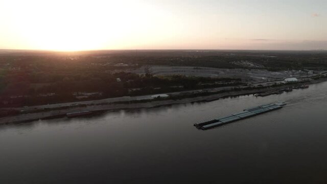 Tugboat pushing barges up Mississippi River at sunset. Aerial static shot.