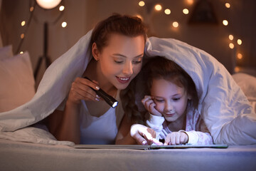 Little girl and her mother with flashlight reading bedtime story
