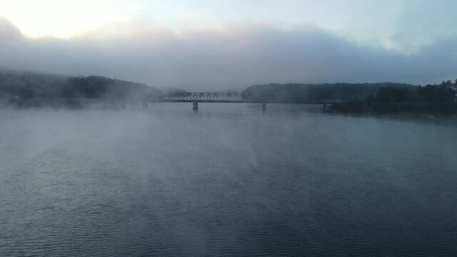 Moving towards a bridge in the mist and fog. Eerie appearance of the bridge through the steam coming off of the water. 4k 30fps.