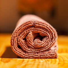 Brown three-ply microfibre tea towel rolled up on a wooden surface