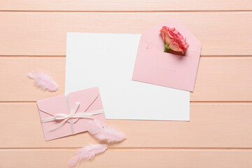 Blank card with envelopes, rose and feathers on pink wooden background