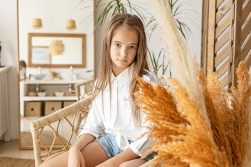 portrait of thoughtful beautiful teenage girl with long hair in white shirt and denim shorts on...