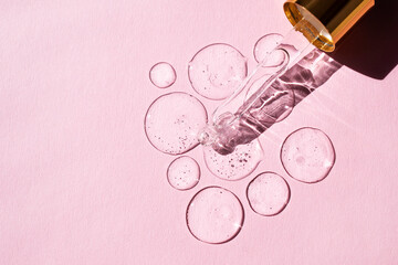 Transparent drops of hyaluronic acid and glass pipette on pink background. Top view, place for text.