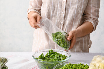 Woman holding plastic bag with frozen green beans on light background, closeup