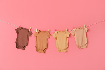 Different baby bodysuits hanging on rope against color background
