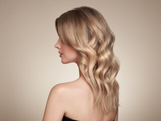Fototapeta premium Blonde woman with long and shiny curly hair. Beautiful model girl with curly hairstyle. Care and beauty hair products