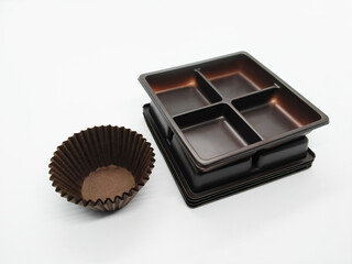 Dark brown empty plastic tray & cupcake baking paper cups on white background.