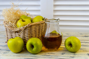 Green apples, basket with apples and jug with apple juice on wooden background