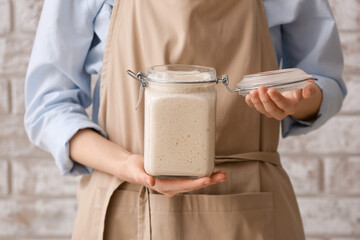 Woman with jar of fresh sourdough near brick wall, closeup