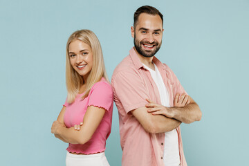 Obraz premium Side view young smiling happy fun couple two friends family man woman in casual clothes stand back to back hold hands crossed together isolated on pastel plain light blue background studio portrait.