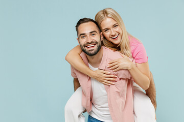 Young couple two friends family man woman in casual clothes giving piggyback ride to joyful, sit on back together isolated on pastel plain light blue color background studio People lifestyle concept.