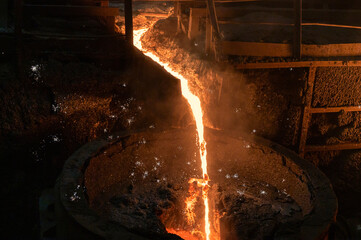 Molten iron. Liquid metal is poured into the ladle in a thin stream.