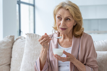 Smiling elderly woman who eats yogurt sitting on the couch