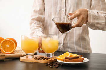 Woman pouring coffee into glass with orange juice on light background, closeup