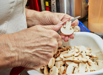 Woman cuts mushrooms on wooden cutting board. Cooks according to the recipe at home in the kitchen