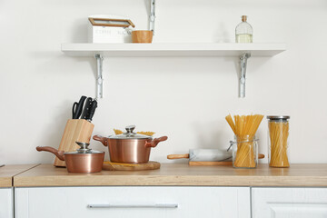 Fototapeta na wymiar Copper cooking pots and jars with raw pasta on kitchen counter near white wall