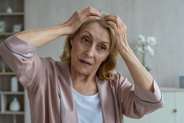 An elderly woman has problems with hair loss. An elderly woman looks at her hair in the mirror and...