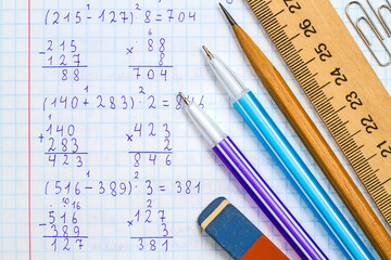 Ruler, pencil, pens, eraser and paper clips on the background of a school notebook in mathematics.