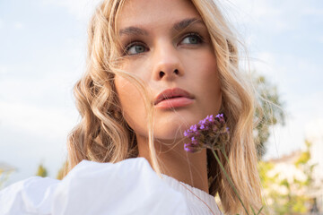 A portrait of a beautiful blond girl holding a purple flower close to her face.