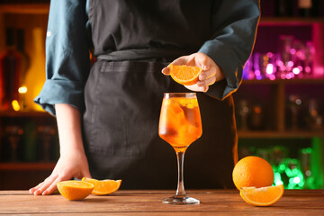 Woman decorating glass of aperol spritz cocktail with orange on dark background