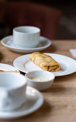 Fresh pancakes with filling on the table next to white mugs for coffee or tea for breakfast. Pancakes for a sweet dessert after lunch in a cozy coffee.