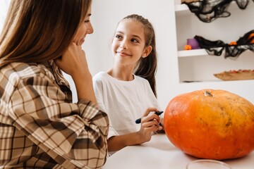 White mother and daughter smiling while making Halloween pumpkin