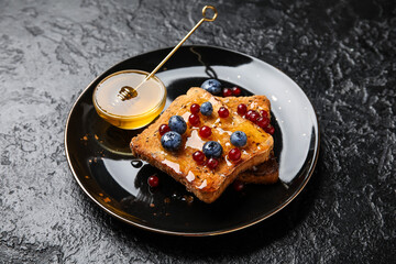 Plate of delicious toasted bread with honey and berries on black background
