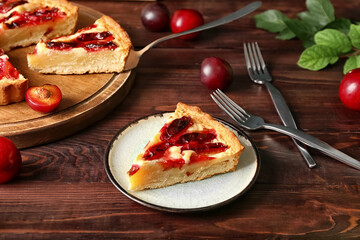 Plate with piece of tasty plum pie on wooden background, closeup