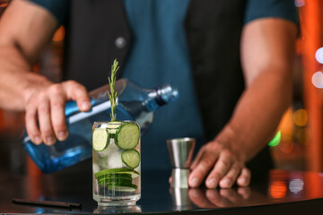 Male bartender making cucumber gin and tonic on table in bar, closeup