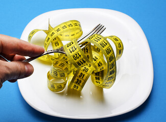 The man is holding a fork in his hand. Measuring tape is wound around the fork. Healthy food,...