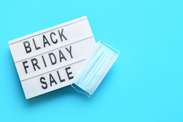 Board with text BLACK FRIDAY SALE and medical mask on color background