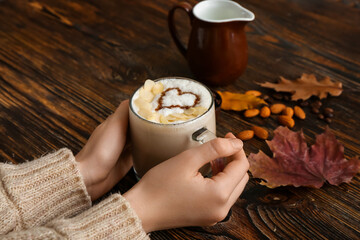 Female hands with cup of tasty almond latte on wooden background