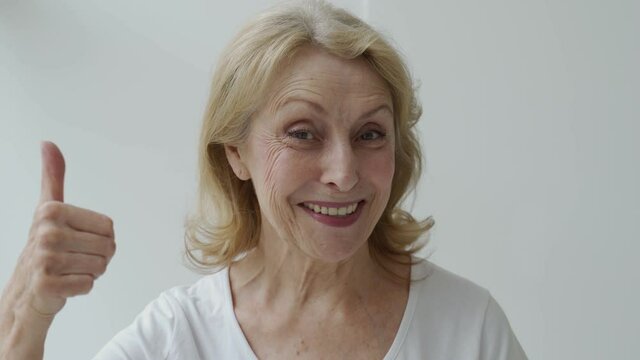 The concept of having strong healthy white perfect teeth in old age. Portrait of an elderly lady with a beaming smile, pointing at her teeth, showing a thumbs up