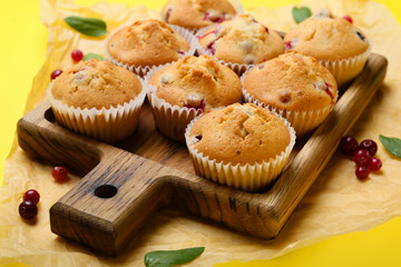 Wooden board with tasty cranberry muffins on color background