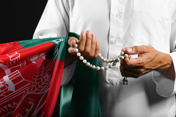 Muslim man with flag of Afghanistan and tasbih on dark background, closeup
