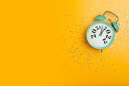 New Year 2022 banner background concept. 2021 changes to 2022 on an alarm clock on a yellow background with festive glitter on New Year's Eve and Christmas.