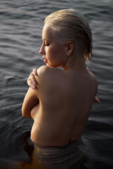 Nude naked sexy woman in water at sunset. Beautiful blonde woman with short wet hair and big...