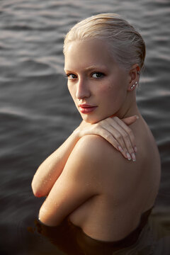 Nude naked sexy woman in water at sunset. Beautiful blonde woman with short wet hair and big breasts, art portrait in sea