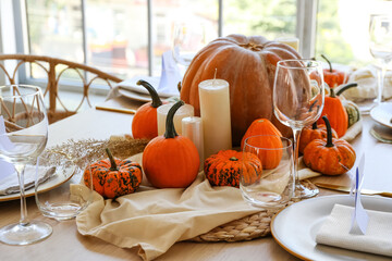 Beautiful autumn table setting with pumpkins and candles in room