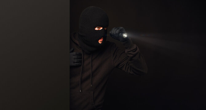 Masked burglar with flashlight on dark back