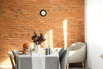 Dining table with pumpkins and flowers near brick wall