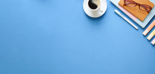 Top view coffee cup, glasses, stationery and notebook on blue background. Copy space.