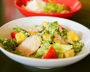 Caesar Salad served in a white bowl on the table in restaurant or diner. Traditional recipe of Caesar salad