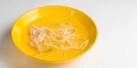 Chicken stock with noodles served in a yellow bowl over white background, isolated on white.
