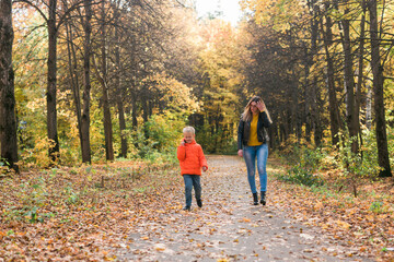 Mother and son walking in the fall park and enjoying the beautiful autumn nature. Season, single parent and children concept.