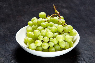 Branch of ripe green grape on plate with water drops. Juicy grapes on wooden background, closeup. Grapes on dark kitchen table with copy space