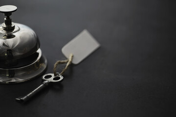 A shiny silver metal bell at the hotel reception. A table in the hotel at the concierge with a bell and a door key. Key and bell in a hotel.