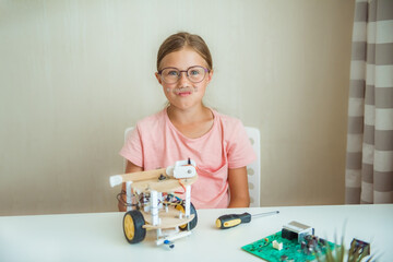 Funny girl constructs robot and program it. The boards and microcontrollers are on the table. STEM...