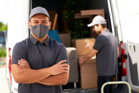 Man with protective face mask standing with arms crossed near moving van