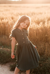 Fototapeta na wymiar Beautiful little girl with long hair walking through a wheat field on a sunny day. Outdoors portrait. Kids relaxing